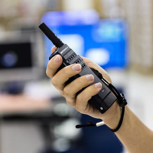 Radiostanice Motorola MOTOTRBO SL1600 VHF v ruce s poutkem na zápěstí, v pozadí rozostřená kancelář.