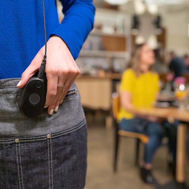Zezadu radiostanice Motorola CLP446e zasunutá v kapse kalhot s připojenou náhlavní sadou.