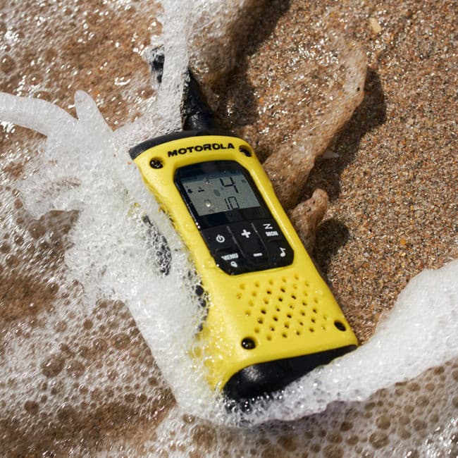 Vysílačka Motorola TLKR T92 H20 PMR446 ležící v písku, omývaná mořskou pěnou, čelní stranou nahoru.