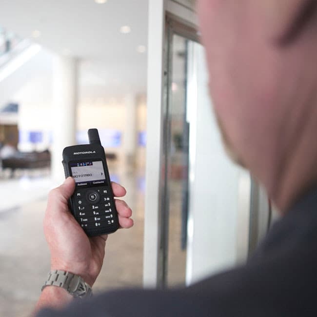 Dospělý muž drží v ruce radiostanici Motorola MOTOTRBO SL4010e s displejem zobrazujícím MOTOTRBO, v pozadí je rozostřená moderní budova.