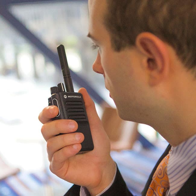 Muž v košili a kravatě s radiostanicí Motorola MOTOTRBO DP3441e v ruce z profilu, připraven k hovoru.