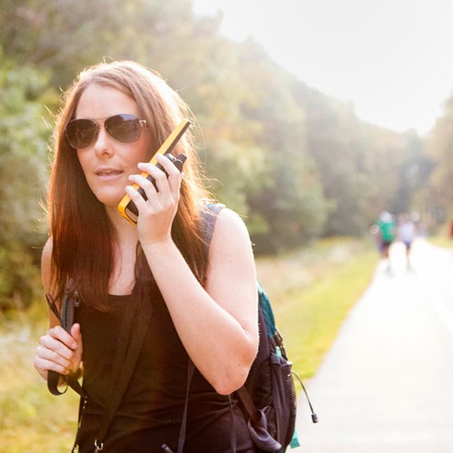 Žena v slunečních brýlích s batohem v přírodě hovoří do radiostanice Motorola TALKABOUT T82 Extreme.